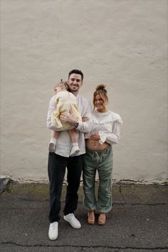 a man and woman standing next to each other with a baby in their arms on the street