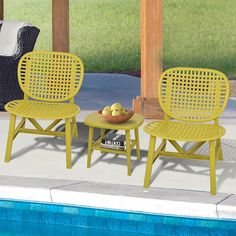 two yellow chairs sitting next to a pool with a bowl of fruit on the table