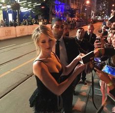 a woman in a black dress signing autographs for fans on the street at night