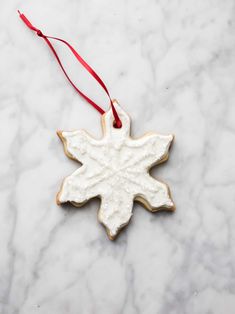 a white snowflake ornament hanging from a red ribbon on a marble surface