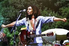 a man standing in front of a microphone with his arms out and holding a guitar