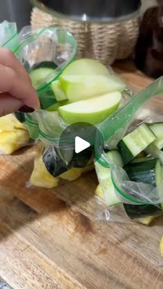 someone is cutting up some vegetables on a wooden board with plastic wrap around the edges