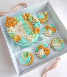 a box filled with lots of cupcakes on top of a white table next to a pink ribbon