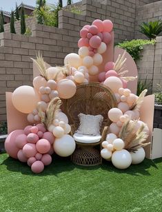 a chair sitting on top of a lush green field covered in balloons and grass next to a brick wall