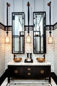 a bathroom with two sinks, mirrors and lights on the wall above them is black and white tile