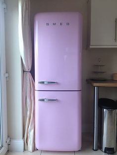 a pink refrigerator sitting in the corner of a kitchen next to a trash can and table