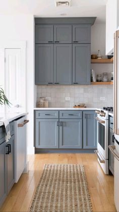 a kitchen with gray cabinets and white counter tops, hardwood floors, and a rug on the floor