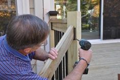 a man using a drill to attach a wooden rail on a deck outside his house