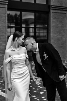 a bride and groom are kissing in front of a building on their wedding day, black and white photo