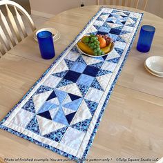 a table runner with fruit on it and blue glass vases next to the plate