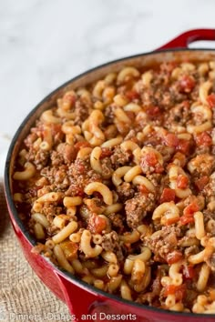 a large red pot filled with pasta and ground beef on top of a wooden table