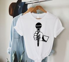 a t - shirt with a microphone on it hanging from a hanger next to clothes