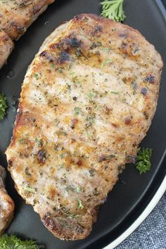 two pork chops on a black plate with parsley sprig garnish