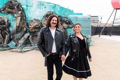 a man and woman standing next to each other in front of a wall with art on it