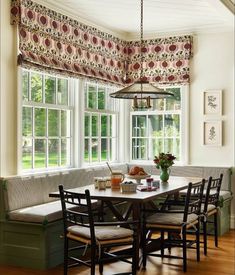 a dining room table with four chairs and a bench in front of the bay window