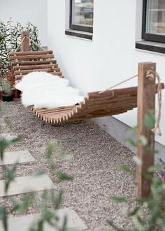 a wooden bench sitting on top of a gravel ground next to a white wall and window