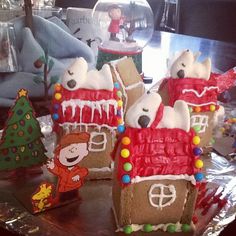 gingerbread houses with frosting and decorations on a table in front of a christmas tree