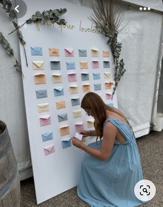 a woman sitting on the ground next to a wall with many different colored envelopes