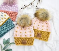 three knitted hats with pom - poms are laying on a white surface