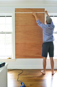 a man is painting the wall in his living room with wood paneling and roller shades