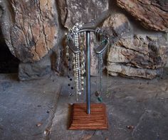 a wooden stand with beads and necklaces hanging from it's sides next to a rock wall