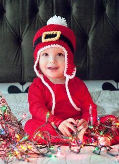 a baby wearing a santa hat sitting on top of a bed next to christmas lights