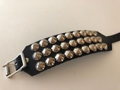 "Black leather studded punk bracelet with 3 rows of cone studs. Cone studs are 1/2\" wide and about 3/8\" tall so bracelet can easily be worn under jacket sleeves. Cone studs are made from high quality nickel plated brass. Buckle and rivets are also nickel plated. Bracelet is 1.75\" wide. Smaller cuff has fewer studs. Made out of hand dyed vegetable tan leather. Ask about custom sizes and colors!" Punk Black Bracelet With Silver Studs, Rocker Leather Bracelet With Rivets For Festivals, Rocker Style Leather Bracelet With Studs For Festivals, Punk Adjustable Cuff Bracelet With Rivets, Punk Style Adjustable Cuff Bracelet With Rivets, Adjustable Punk Cuff Bracelet With Rivets, Metal Spiked Leather Bracelet For Parties, Punk Leather Bracelet With Studs For Festivals, Metal Studded Bracelets For Concerts