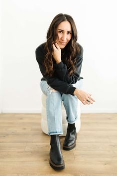 a woman sitting on top of a white chair next to a wooden floor and wearing black boots