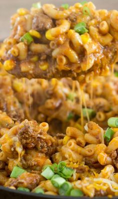 a skillet full of macaroni and cheese being lifted with a wooden spoon