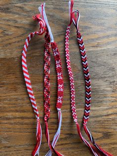 three red, white and black braided necklaces on a wooden table with one knot tied to the other