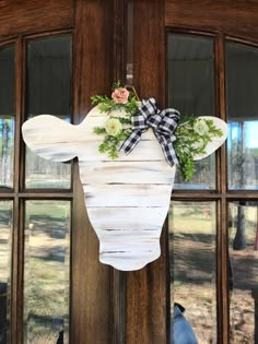 a wooden moose head hanging on the front door with flowers and greenery attached to it