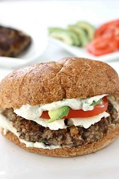 a close up of a sandwich on a plate with tomatoes and cucumbers in the background