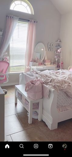 a white bed sitting in a bedroom next to a window with pink curtains and pillows