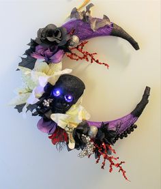 a purple and black wreath with flowers on the front, decorated with skulls and leaves