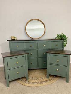 the dressers are painted green and have brass knobs on each drawer, along with a round mirror above them