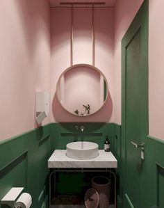 a pink and green bathroom with a round mirror above the sink, toilet paper roll holder on the wall