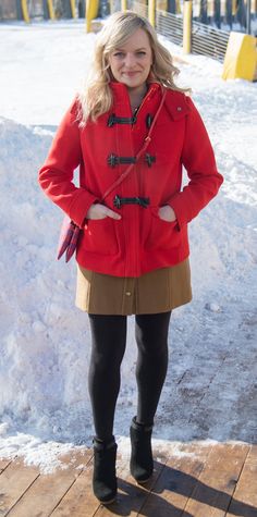 a woman standing in the snow wearing a red coat and black boots with her hands on her hips