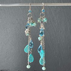 Long turquoise colored dangle drop statement earrings with various shaped ocean coloured blue beaded clusters in silver. I have meticulously wire wrapped these boho earrings on a long tarnish resistant stainless steel chains with etched blue magnesite leaves, blue faceted Swarovski crystal briolettes, blue etched Czech hexagonal chandelier beads and etched silver plated flowers with gorgeous blue cubic zirconia bezel set fish hooks in 925 sterling silver which is hypoallergenic and good for sens Turquoise Dangle Earrings With Ocean-inspired Style, Turquoise Dangle Earrings Ocean-inspired, Ocean-inspired Turquoise Dangle Jewelry, Blue Bohemian Jewelry With Dangling Charms, Blue Wire Wrapped Dangle Chandelier Earrings, Blue Drop Earrings With Dangling Charms, Blue Wire Wrapped Chandelier Earrings, Blue Bohemian Beaded Sterling Silver Earrings, Bohemian Blue Beaded Sterling Silver Earrings