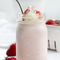 a strawberry milkshake in a mason jar with strawberries around it on a white surface