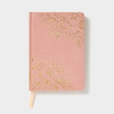 a pink notebook with gold foil flowers on the cover and a wooden stick sticking out of it