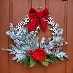 a christmas wreath on the front door with red and white flowers, pine cones and evergreens