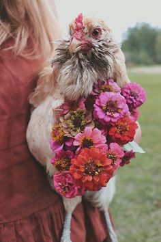 a woman holding a bouquet of flowers with a chicken on her arm in the background