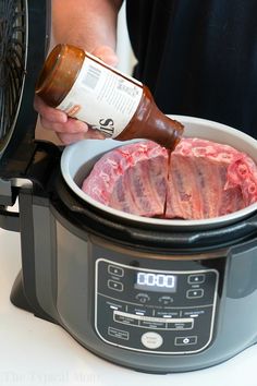 a person pouring sauce into a slow cooker with raw meat in the bowl on top