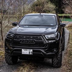 the front end of a black truck parked on a dirt road next to some trees