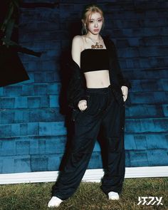 a woman standing in front of a blue wall wearing black pants and cropped top