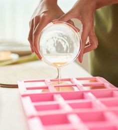 a person pouring liquid into a glass on top of a pink tray filled with squares