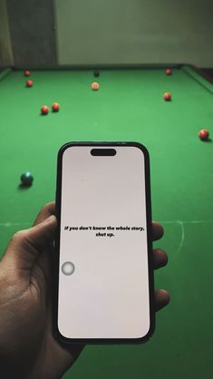 a person holding up an iphone in front of a pool table with balls on it