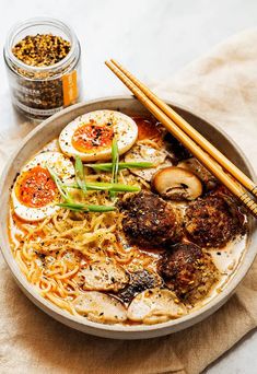 a bowl filled with noodles, meat and veggies next to chopsticks