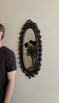 a man standing in front of a wall with a flower vase on it and a mirror hanging on the wall