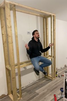 a man standing on top of a wooden frame in the middle of a room that is being built